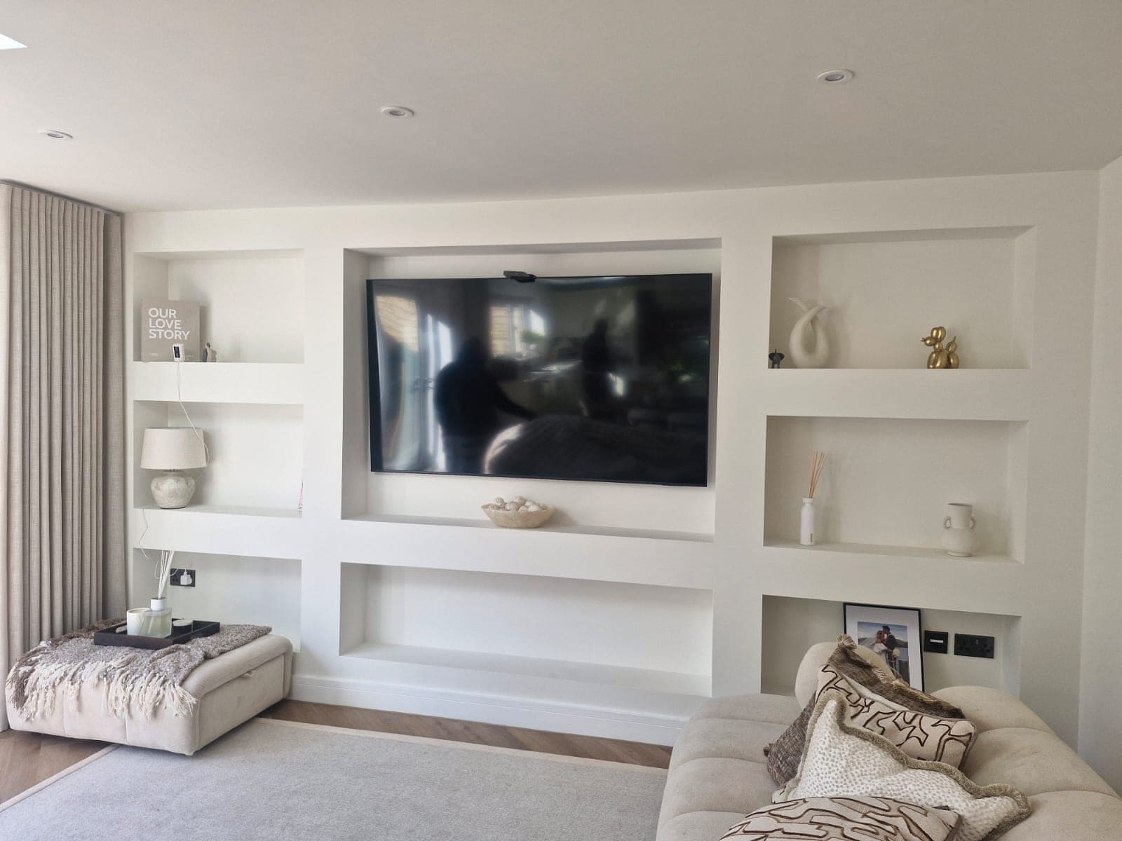 The original media wall before the renovation: flat white painted niches with the television surface-mounted and open shelves either side