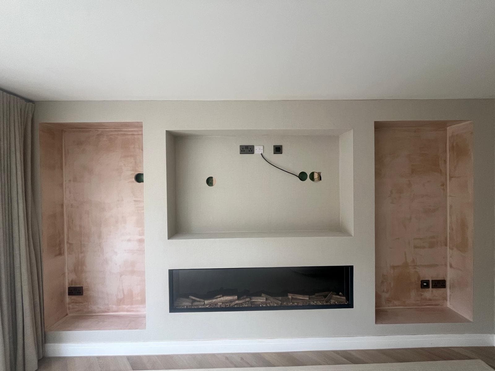The media wall in bare plaster, with the three openings formed, the electric fire fitted and cabling run into the television opening