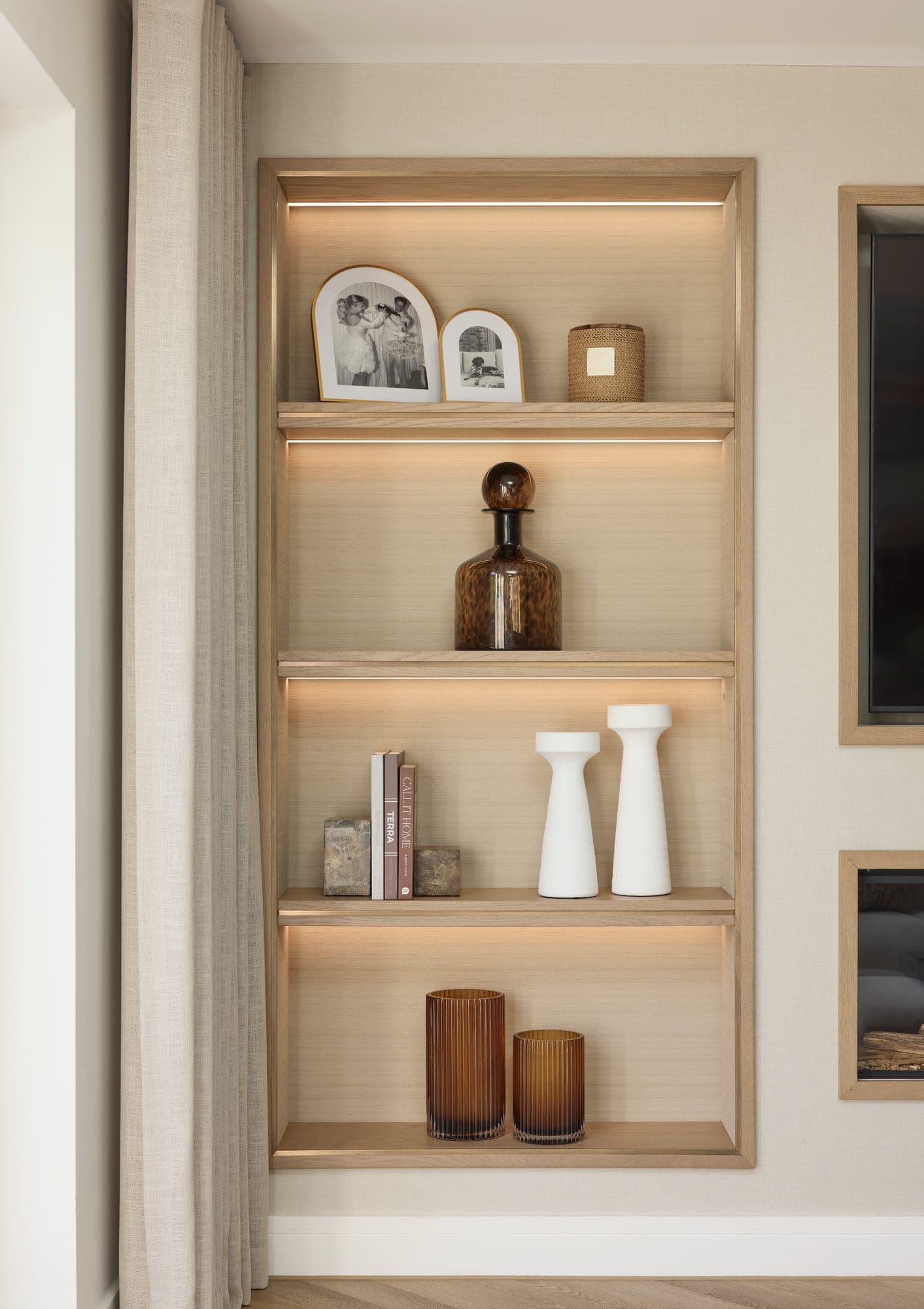 The full-height lit alcove shelving beside the television, styled with framed photographs, an amber vessel and candlesticks