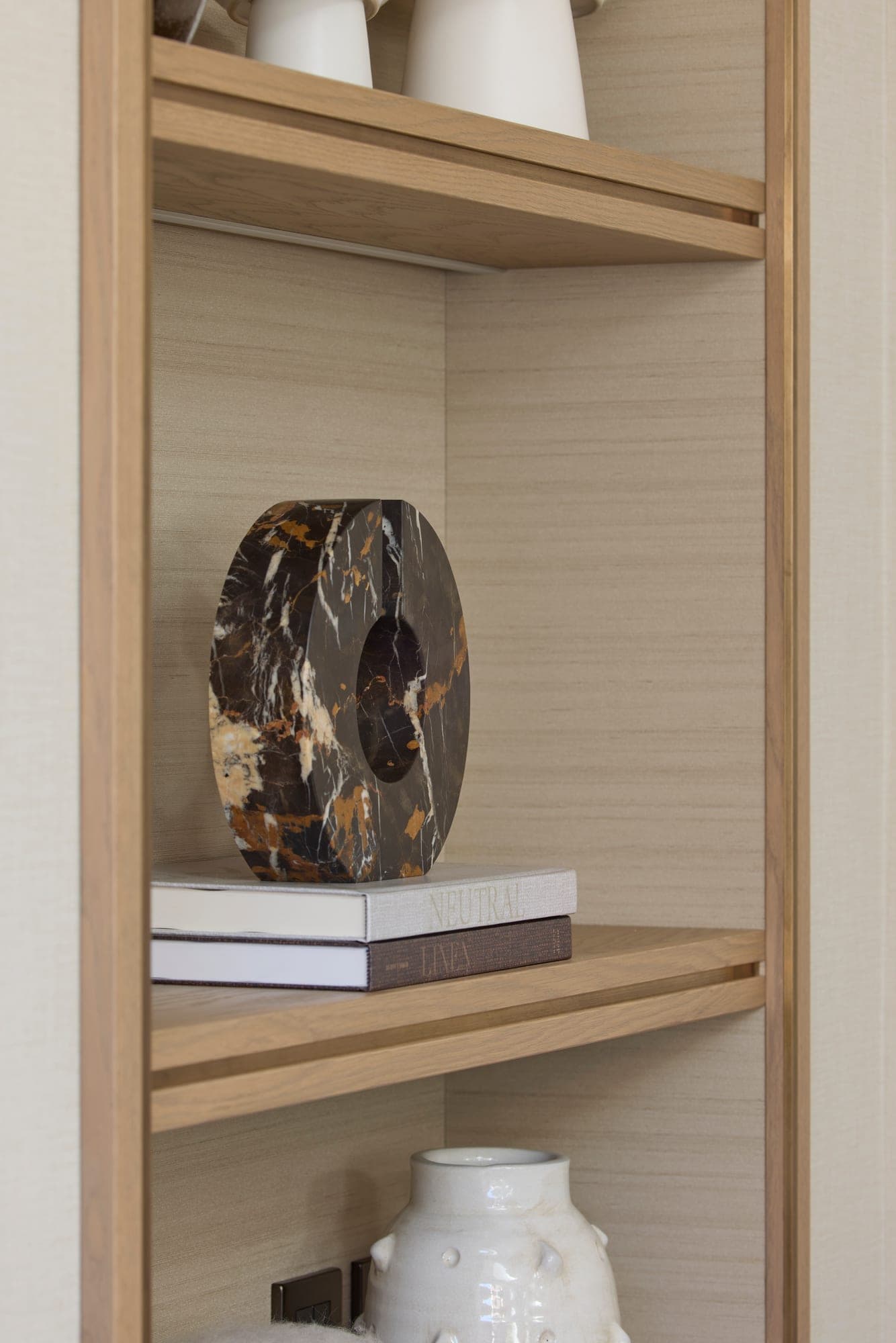 A fossil marble disc resting on stacked books on a lit oak shelf
