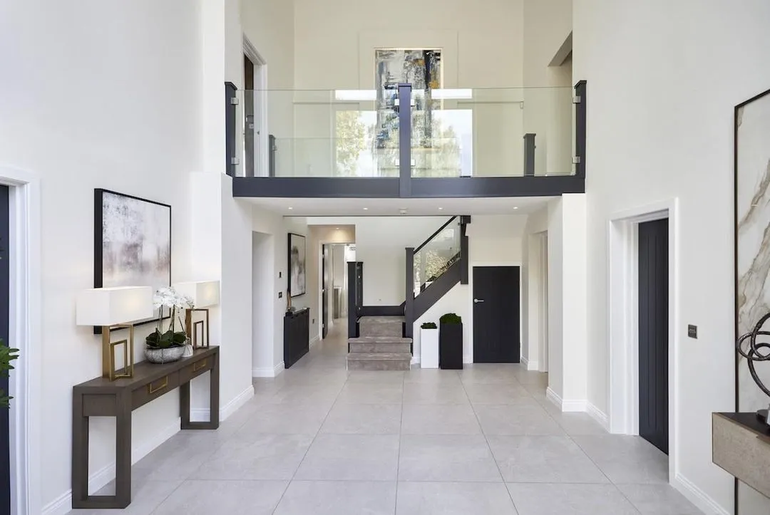 A generous, double-height hall kept warm and welcoming with a console, lamps and a runner